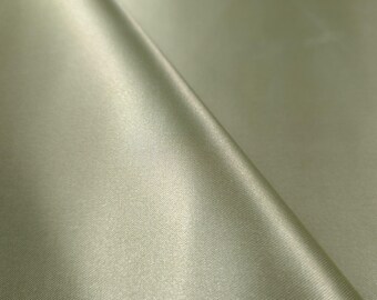 May include: Close-up of a folded piece of fabric in a pale green color. The fabric has a smooth, satin-like texture with subtle sheen. The folds create shadows and highlights, adding depth to the image. The fabric appears to be lightweight and flowing.