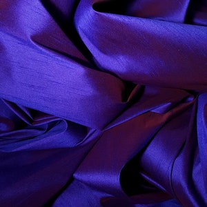 K&ouml;nnte beinhalten: Nahaufnahme eines tiefvioletten Stoffes mit seidenartiger Textur. Der Stoff ist gefaltet und drapiert und erzeugt weiche, flie&szlig;ende Linien.