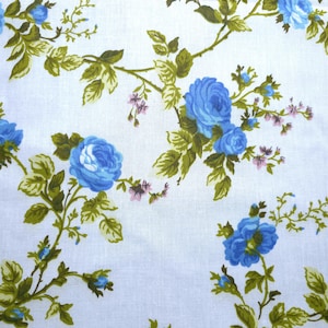 May include: White fabric with a repeating pattern of blue roses, green leaves, and small pink flowers. The floral design is spread across the fabric, creating a vintage or cottagecore aesthetic.