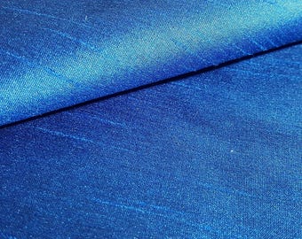 May include: Close-up of a vibrant blue fabric with a subtle sheen. The material is folded, creating a diagonal line across the image. The texture appears smooth with slight variations in color, adding depth to the textile.
