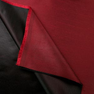 May include: A close-up of a piece of fabric, showcasing a rich, two-toned design. The top layer is a deep red, while the underside reveals a contrasting black. The edges are frayed, adding texture to the material.