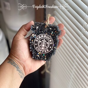 May include: Black glitter air freshener in the shape of a Starbucks coffee cup. The Starbucks logo is in the center. The air freshener has a jute string for hanging. The text "Triple R Freshies" is in the background.