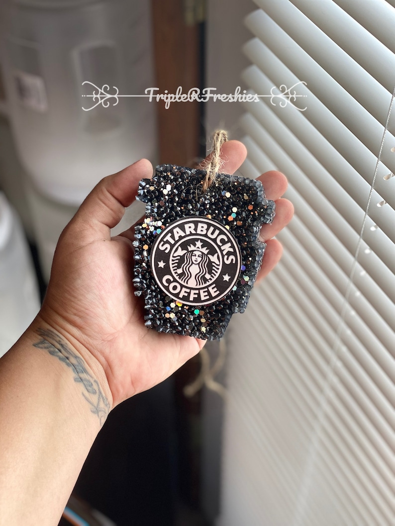 May include: Black glitter air freshener in the shape of a Starbucks coffee cup. The Starbucks logo is in the center. The air freshener has a jute string for hanging. The text "Triple R Freshies" is in the background.