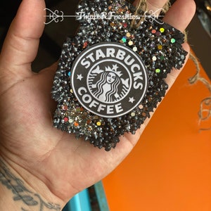 May include: A black, glitter-covered air freshener in a leaf shape, featuring the Starbucks Coffee logo. The air freshener has a jute string for hanging and the text "Triple R Freshies".