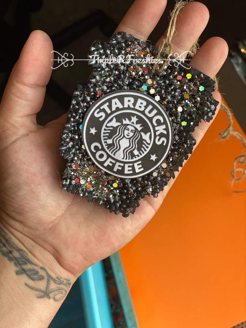 May include: A black, glitter-covered air freshener in a leaf shape, featuring the Starbucks Coffee logo. The air freshener has a jute string for hanging and the text "Triple R Freshies".