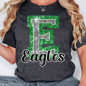 May include: Green and silver glitter letter E with the word "Eagles" in black script below. The letter and word are on a dark gray t-shirt.