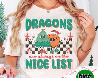 Puede incluir: Una camiseta blanca con un diseño gráfico verde y rojo que presenta un árbol de Navidad y una galleta con el texto "DRAGONS siempre están en la LISTA DE BUENOS".