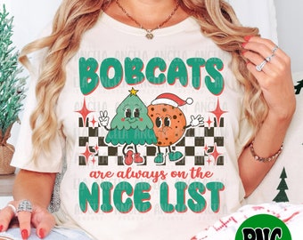 May include: White t-shirt with a green and red graphic of a Christmas tree and a cookie with the text "Bobcats are always on the nice list".