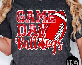 Peut inclure: T-shirt gris foncé avec l'inscription "GAME DAY Bulldogs" en rouge et blanc, ainsi qu'un ballon de football rouge. Le texte a un effet scintillant. Le t-shirt est à col rond.