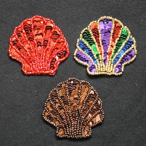 Può includere: Tre toppe a forma di conchiglia con paillettes rosse, multicolori e marroni. La conchiglia rossa è di colore pieno, mentre la conchiglia multicolore ha un arcobaleno di colori. La conchiglia marrone è un mix di paillettes marroni e dorate.