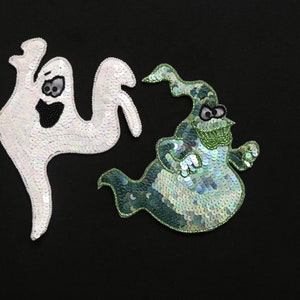 May include: Two Halloween ghost appliqu&eacute;s on a black background. One is white with black bead details, the other is green and blue with bead and sequin details. The appliqu&eacute;s are whimsical and decorative.