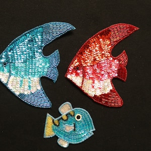 May include: Three colorful fish-shaped patches made of sequins. The fish are blue, red, and pink. The blue fish are in the shape of an angelfish, while the red and pink fish are in the shape of a goldfish.