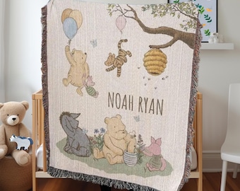 May include: A cream-colored woven baby blanket with a Winnie the Pooh theme. The blanket features Winnie the Pooh, Piglet, Tigger, and Eeyore. The blanket also has a beehive, balloons, and flowers. The blanket is personalized with the name "Noah Ryan".