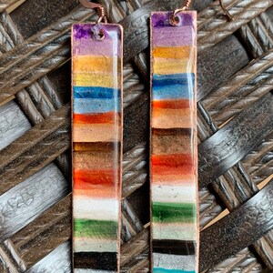 May include: A pair of long, rectangular earrings with a copper wire frame and colorful glass tiles. The tiles are arranged in horizontal stripes of purple, gold, blue, orange, brown, white, green, black, silver, and turquoise.