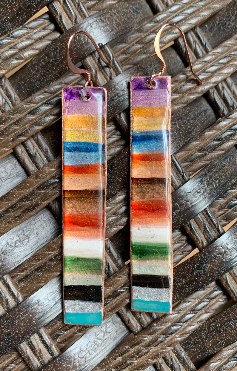 May include: A pair of long, rectangular earrings with a copper wire frame and colorful glass tiles. The tiles are arranged in horizontal stripes of purple, gold, blue, orange, brown, white, green, black, silver, and turquoise.