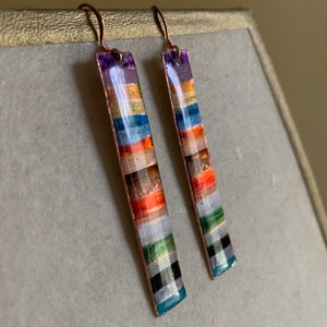 May include: A pair of long, rectangular earrings with a copper wire frame and colorful, layered, rectangular pieces of glass or stone. The earrings have a copper wire hook.