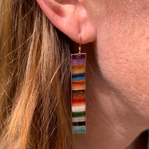 May include: A pair of long, colorful dangle earrings with a copper wire hook. The earrings are made of a variety of colorful stones and are arranged in a vertical stripe pattern.