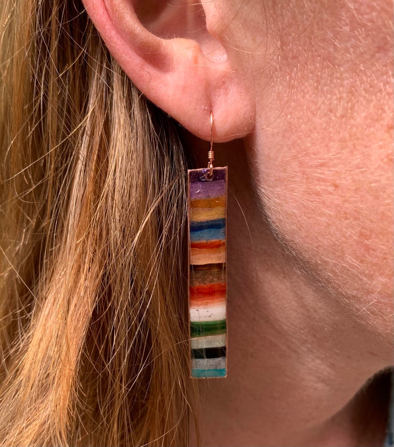 May include: A pair of long, colorful dangle earrings with a copper wire hook. The earrings are made of a variety of colorful stones and are arranged in a vertical stripe pattern.