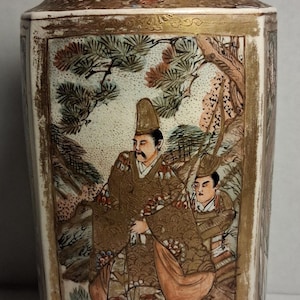 Puede incluir: Jarrón japonés antiguo con base crema y parte superior acampanada. El jarrón presenta obras de arte detalladas de figuras con vestimenta tradicional, sobre un fondo de árboles y follaje, con detalles dorados. Objeto decorativo.