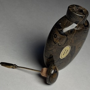 Op de afbeelding: Een bruine en zwarte marmerachtige fles met een bijpassende stopper en een goudkleurige applicator. De fles heeft een afgeronde vorm en een kleine opening aan de bovenkant. De applicator is gemaakt van goudkleurig metaal en heeft een klein, plat uiteinde. De fles heeft een sticker met "Made in China".