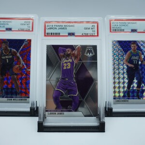 May include: Three graded basketball trading cards in protective cases. The cards feature Zion Williamson, LeBron James, and Luka Dončić. The cards are from the 2019 Panini Mosaic series.