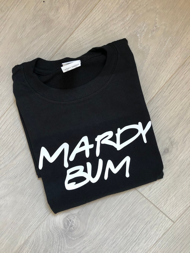 May include: Black t-shirt with white text that says "Mardy Bum".