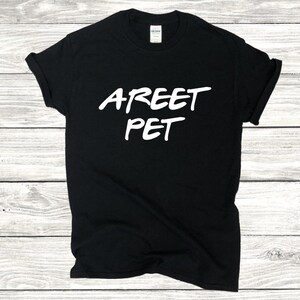 May include: Black t-shirt with the white text "AREET PET" in a handwritten style. The shirt is made of a soft material and has short sleeves. The shirt is displayed on a light wood grain surface.