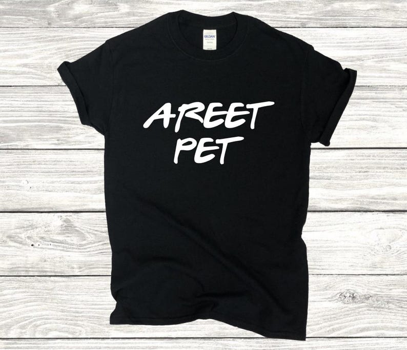 May include: Black t-shirt with the white text "AREET PET" in a handwritten style. The shirt is made of a soft material and has short sleeves. The shirt is displayed on a light wood grain surface.