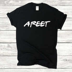 May include: Black t-shirt with the white word "AREET" in a handwritten style. The shirt is made of a soft material and has a classic crew neck. The image is taken on a light wood grain background.