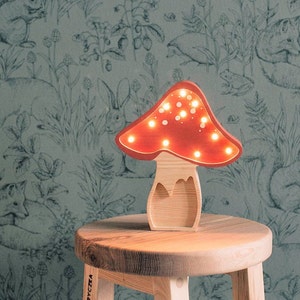 May include: A mushroom-shaped lamp with a light wood base and a red cap featuring small, circular cutouts that emit a warm, glowing light. The lamp is constructed from wood and is designed to stand upright on a flat surface, showcasing a natural grain.