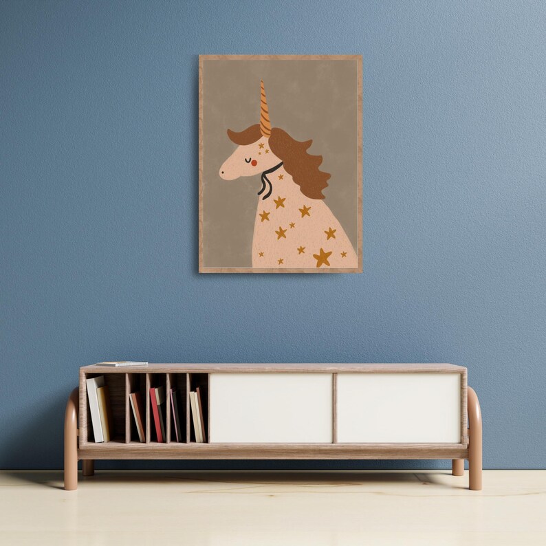May include: A framed print featuring a whimsical unicorn illustration. The unicorn has a light pink body adorned with gold stars, a brown mane, and a golden horn. The artwork is set against a muted gray background, with a wooden frame.