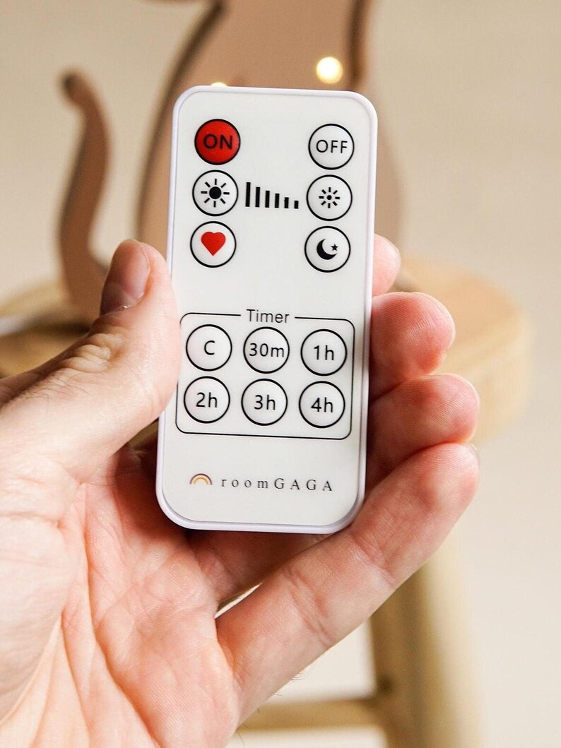 May include: A white remote control with black and red buttons and icons, including "ON", "OFF", a sun, a heart, and a moon. The remote has timer settings and the text "room GAGA".