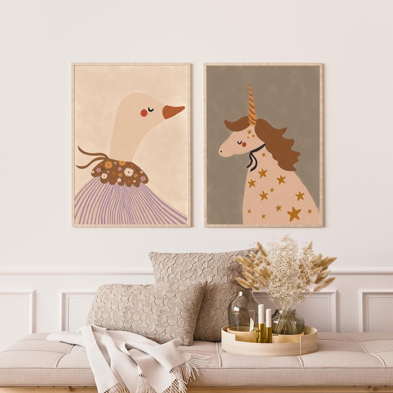 May include: Two framed art prints. One features a goose in a lavender dress with a floral collar. The other depicts a unicorn with a golden horn and star patterns. The prints are displayed above a beige bench with pillows and decorative items.