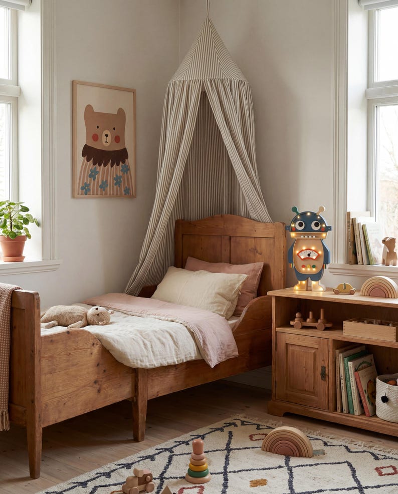 May include: A child's bedroom with a wooden bed, a framed bear illustration, and a robot-shaped lamp. The bed has pink and cream bedding. A striped canopy hangs above the bed. A wooden bookshelf holds toys and books. A patterned rug covers the floor.