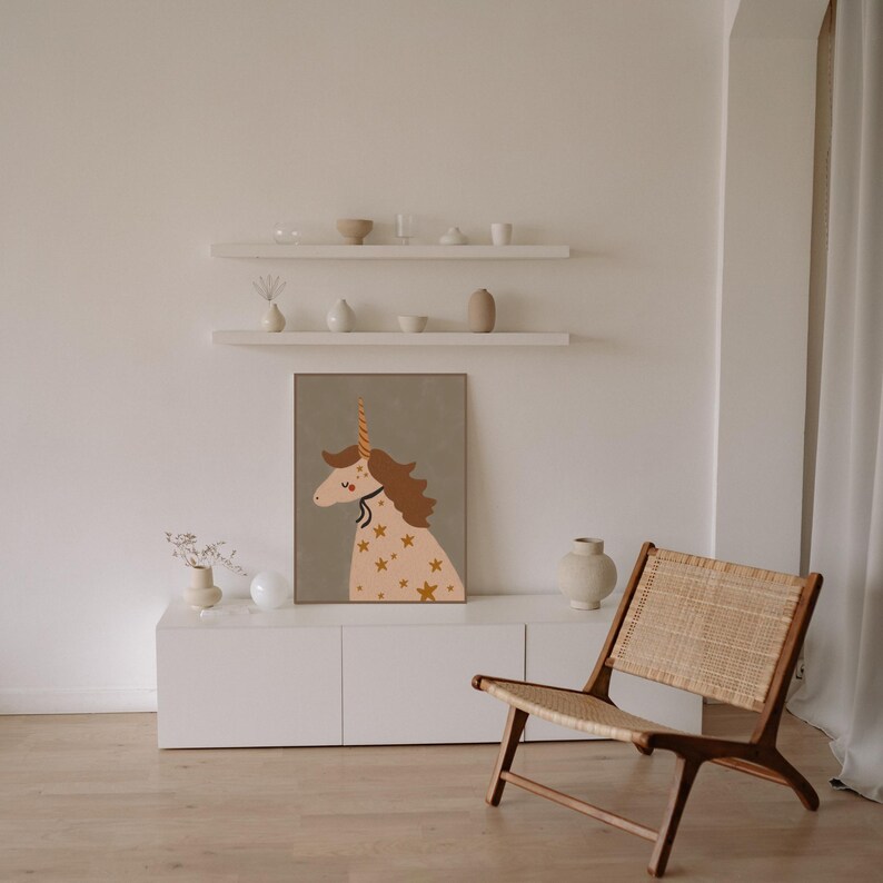 May include: A framed unicorn art print with a gold horn and star accents hangs above a white cabinet. A wooden chair with a woven seat sits nearby. The room has a neutral color palette.