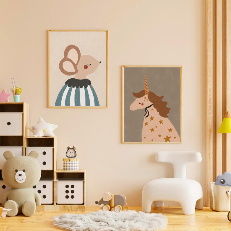 May include: Two framed art prints featuring whimsical animal illustrations. One print shows a mouse with large ears and a blue and white striped outfit. The other print depicts a unicorn with a golden horn and star accents, set against a gray background.