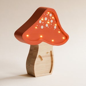 May include: A mushroom-shaped lamp with a light orange cap featuring white circular cutouts and integrated warm LED lights. The base is constructed from light-colored wood with a visible grain pattern, forming a sturdy, upright structure.