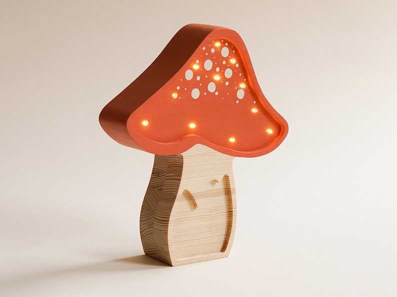 May include: A mushroom-shaped lamp with a light orange cap featuring white circular cutouts and integrated warm LED lights. The base is constructed from light-colored wood with a visible grain pattern, forming a sturdy, upright structure.