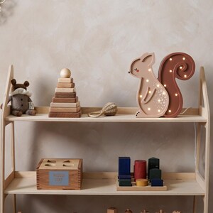 May include: Wooden toy shelf with various children's toys. Includes a light-up squirrel, stacking rings, a wooden box, and other wooden blocks. The shelf is made of light-colored wood.