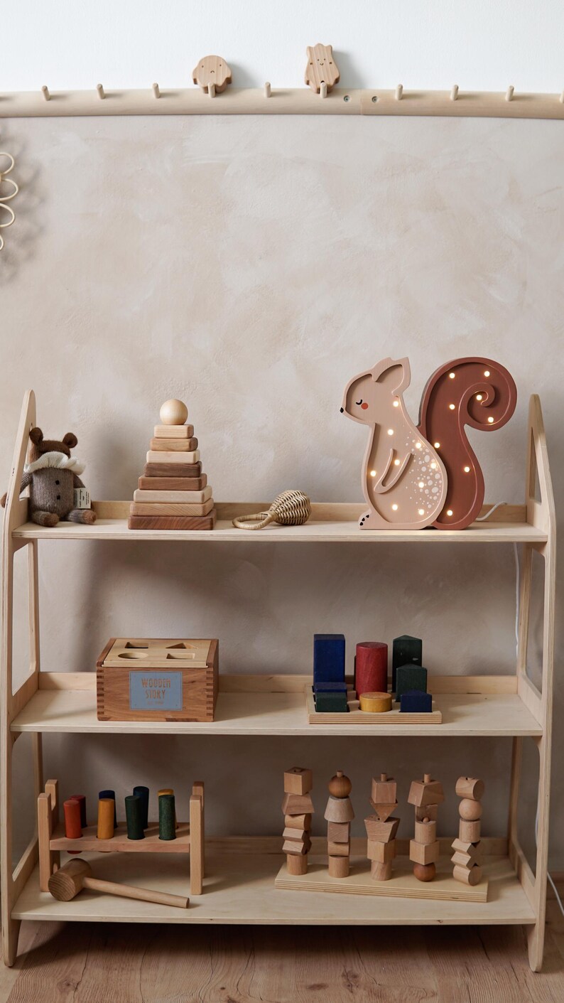 May include: Wooden toy shelf with various children's toys. Includes a light-up squirrel, stacking rings, a wooden box, and other wooden blocks. The shelf is made of light-colored wood.