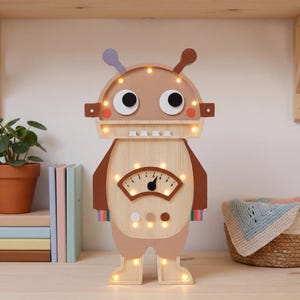 May include: A wooden robot-shaped night light with a light brown body, brown arms, and a light-up face. The robot has a gauge on its chest and small lights throughout. The robot is standing on a wooden surface.