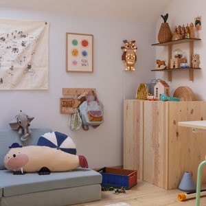 May include: A child's room with a light blue sofa, a walrus-shaped pillow, and a wooden cabinet. The walls are decorated with a world map, a framed artwork, and a wooden light fixture. Toys and decorative items are on shelves.