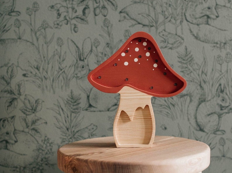 May include: A wooden mushroom-shaped lamp with a red cap featuring white circular spots and small embedded lights. The stem is made of light-colored natural wood with a visible grain, and the overall structure is hollowed out to form a decorative piece.