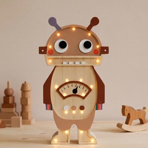May include: A wooden robot-shaped night light with a light brown body, brown accents, and a light-up face. The robot has large black eyes, a meter-like display, and small lights around the head and feet. A fun, decorative item for a child's room.