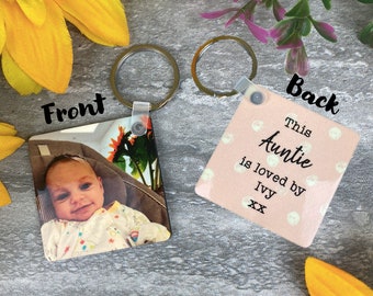 Może przedstawiać: Kwadratowy brelok w kolorze różowym i białym ze zdjęciem dziecka z przodu i tekstem "This Auntie is loved by Ivy xx" z tyłu.