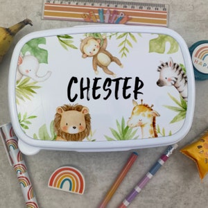 Puede incluir: Fiambrera blanca con tem&aacute;tica de animales de la selva. Presenta un mono, un elefante, un le&oacute;n, una jirafa y una cebra, junto con el nombre "CHESTER" en letras negras. Hojas y follaje verdes rodean a los animales.