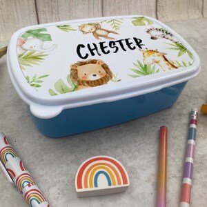 Puede incluir: Una fiambrera azul con tapa blanca decorada con animales de la selva y el nombre "CHESTER". La tapa presenta un le&oacute;n, un mono, una jirafa, un elefante y una cebra, rodeados de follaje verde. Ideal para ni&ntilde;os.