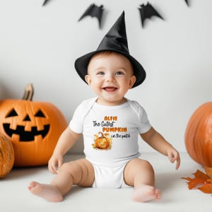 May include: A smiling baby wearing a black witch's hat and a white onesie with the text "Alfie The Cutest Pumpkin in the patch" and a pumpkin graphic. Carved pumpkins and bat decorations are in the background.