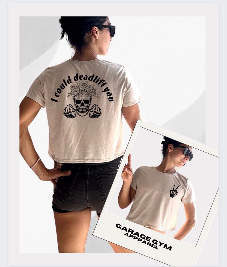 May include: A beige cropped t-shirt with a skull and barbell graphic on the back. The graphic says "I could deadlift you". The shirt is being worn by a person. The front of the shirt has a peace sign graphic. The shirt is from Garage Gym Apparel.