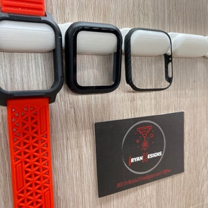 May include: Three black Apple Watch cases, one with a red silicone band, are displayed on a white wall with a business card that reads "RYAN DESIGNS 3D Printed Designs and Gifts".